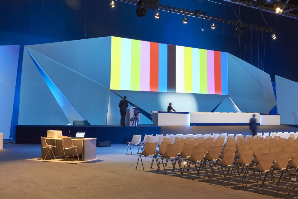 Conferentiezaal met podium, scherm en professionele beeld- en geluidsoplossingen voor vergaderingen, klaar voor een zakelijke presentatie.