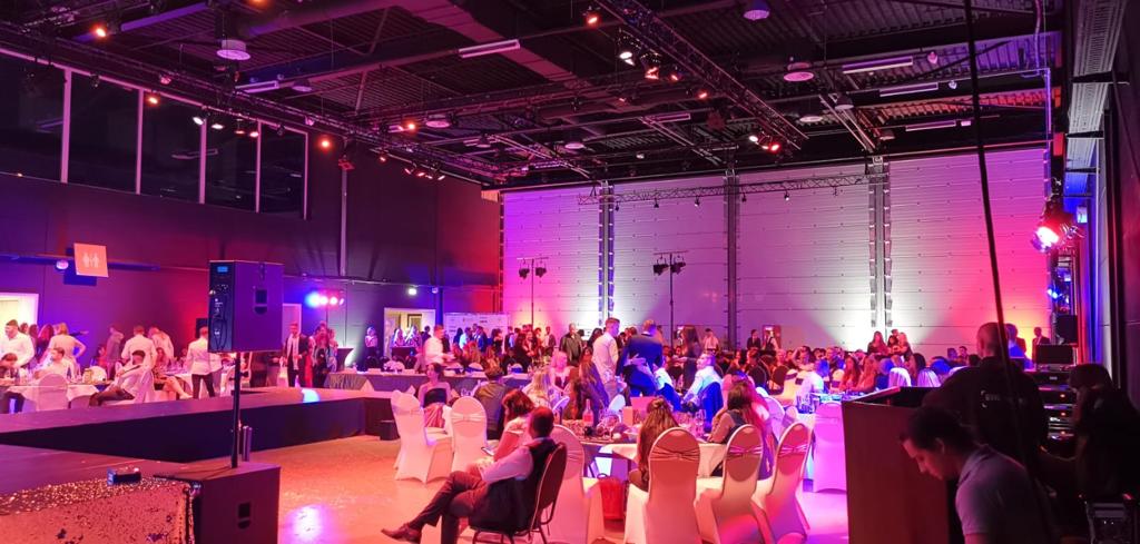 Evenementenzaal voorzien van professionele audiovisuele oplossingen, inclusief verlichting en geluidsinstallaties, tijdens een bedrijfsbijeenkomst met gasten aan tafels en een podiumopstelling.