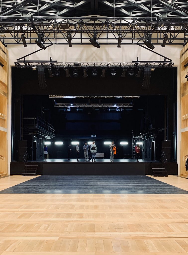Leeg theaterpodium met professionele verlichting en geluidsinstallaties, met technici en crew bezig met de voorbereidingen voor een evenement.