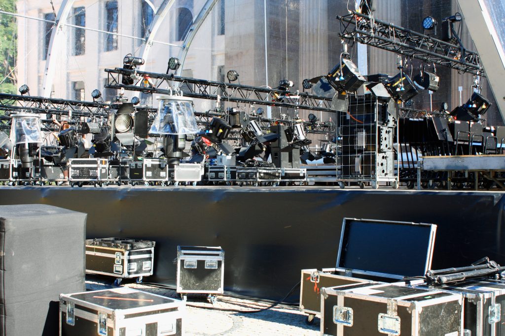 Professionele licht- en geluidsapparatuur op een podium tijdens de voorbereiding van een evenement, inclusief lichtinstallaties, flightcases en trussen.