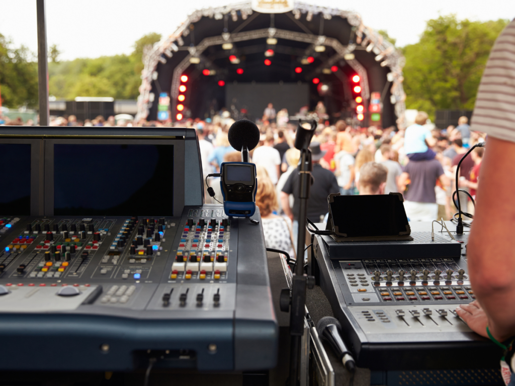 Geluidsinstallatie en mengpanelen opgesteld tijdens een groot festival, met een actief publiek en een podium op de achtergrond. Ideaal voorbeeld van een professioneel geluidssysteem voor evenementen.