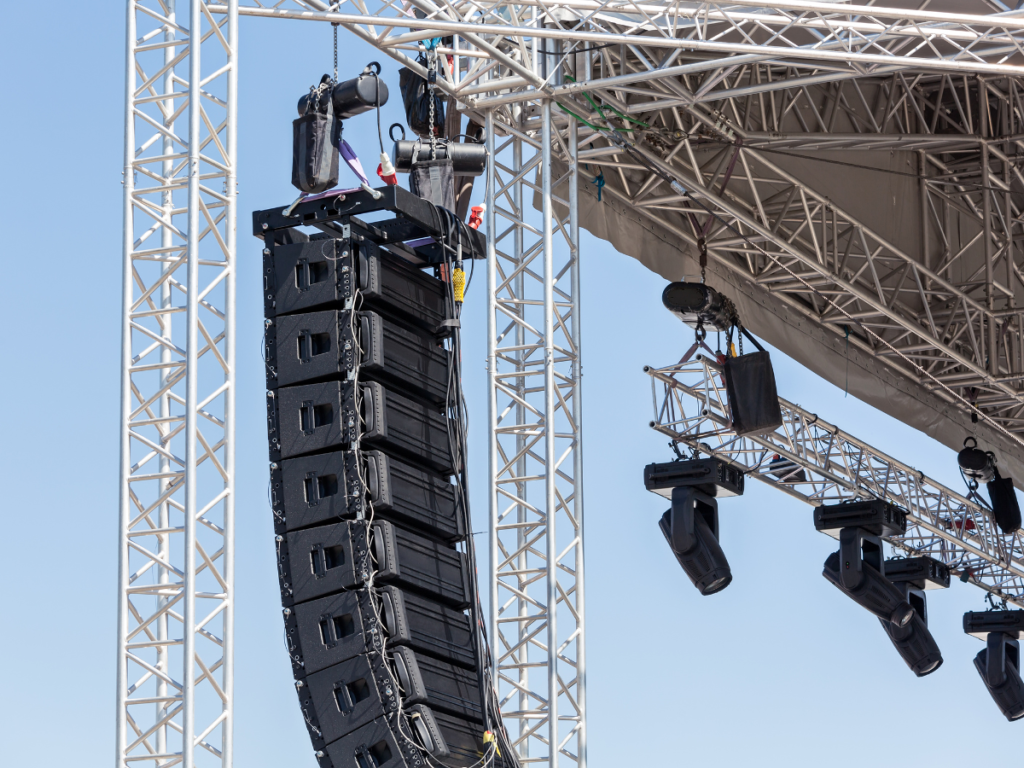 Professioneel line array geluidssysteem voor evenementen, opgehangen aan een stevig podiumframe tijdens een openluchtconcert. Dit systeem zorgt voor optimale geluidsverspreiding op grote locaties.