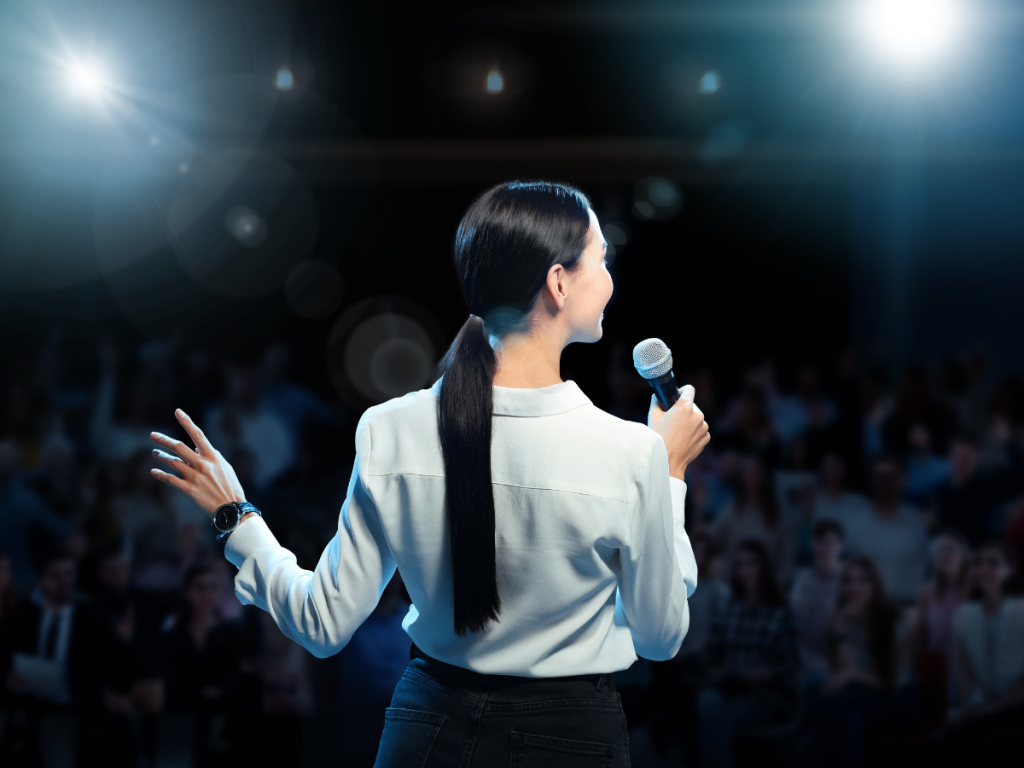 Close-up van een microfoon op het podium tijdens een audiovisuele productie evenement. De zaal is sfeervol verlicht, klaar voor een professionele presentatie.