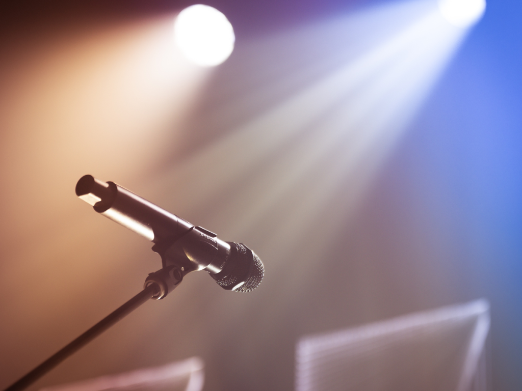 Professionele microfoon in spotlight op een podium, perfect afgestemd voor artiesten dankzij hoogwaardige licht- en geluidsoplossingen.