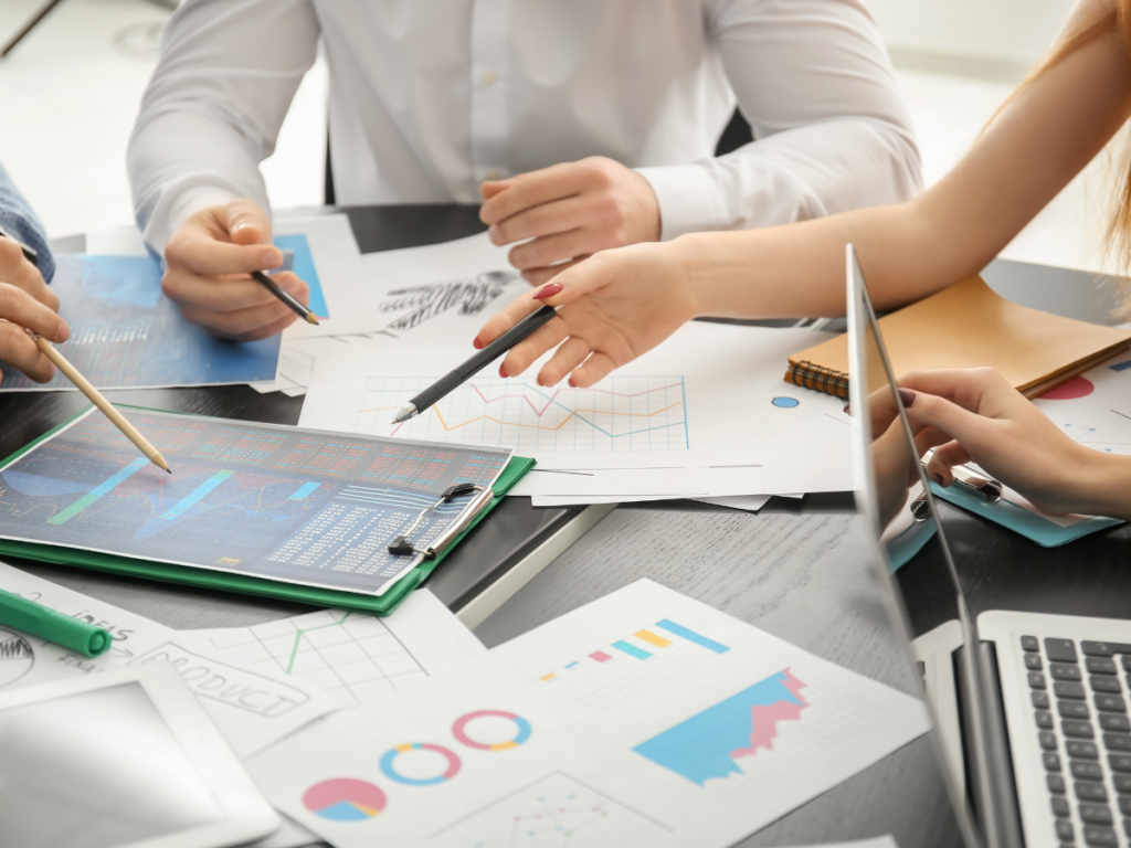 Een team van professionals bespreekt strategieën en analyseren gegevens aan een vergadertafel vol met grafieken, laptops en notitieblokken. Deze setting benadrukt de essentie van zakelijke planning en besluitvorming. Voor evenementenplanning, licht- en geluid huren of audiovisuele ondersteuning is een grondige voorbereiding cruciaal om een vlekkeloze uitvoering te garanderen.