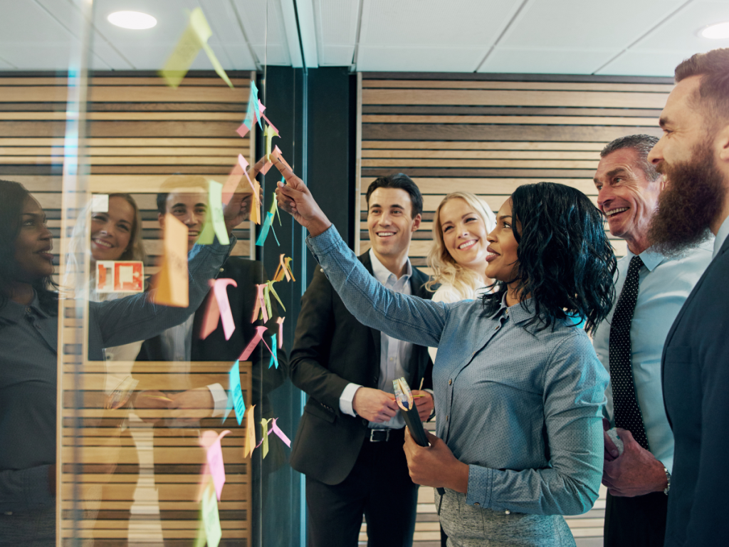 Team brainstormt samen met post-its op glazen wand in creatieve vergaderruimte