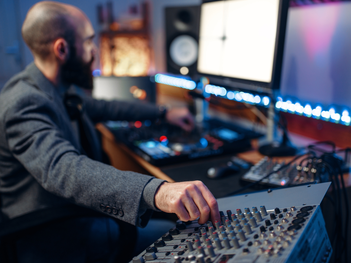Geluidstechnicus werkt aan een mengpaneel in een studio met meerdere monitoren en apparatuur