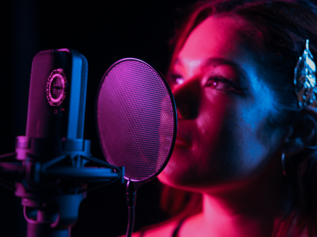 Vrouw zingt in microfoon met popfilter in studioverlichting met roze en blauwe tinten